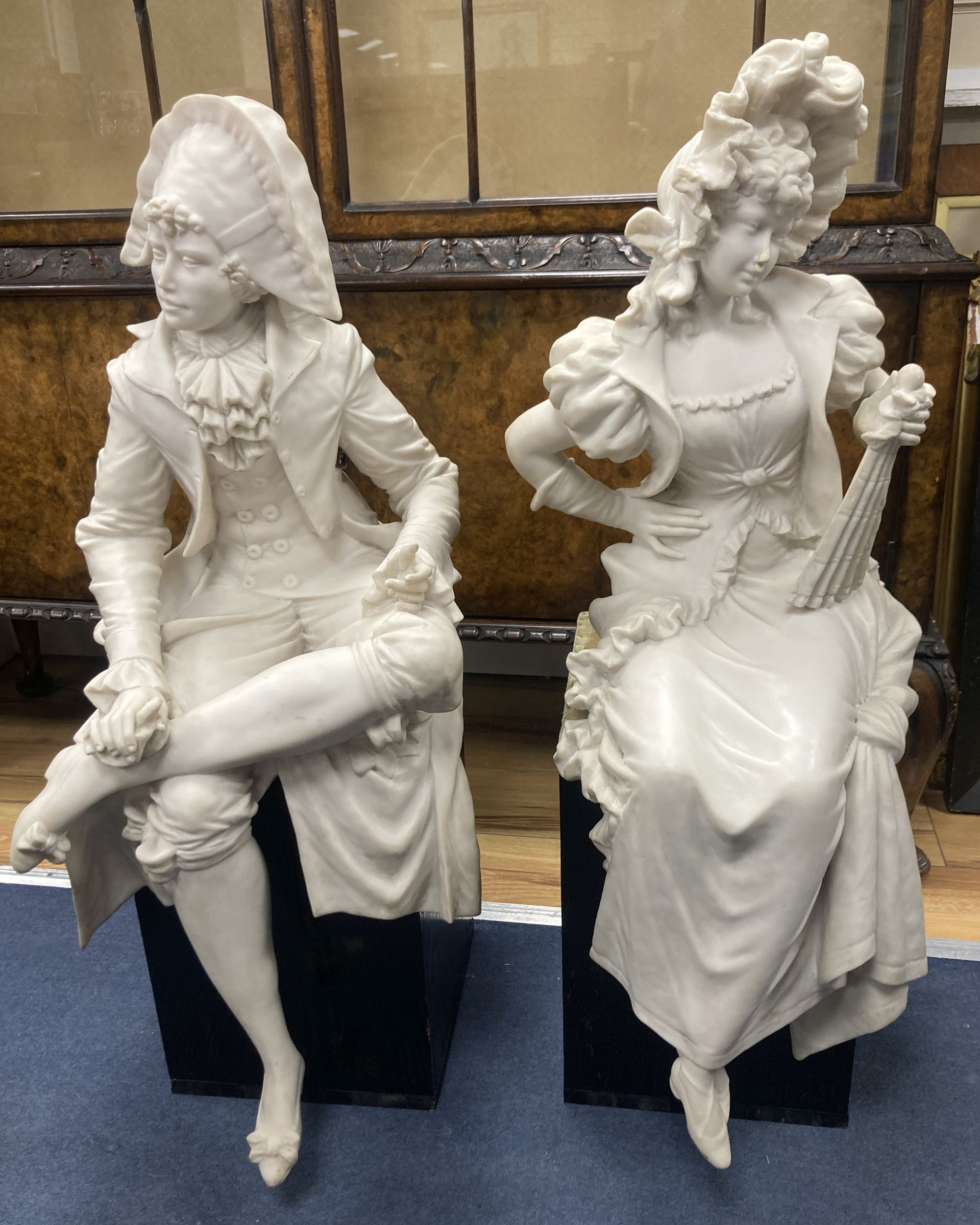 A pair of resin marble seated figures of a Dandy and a Dandizette on ebonised plinths